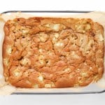 Baked apple cake in a rectangular glass dish lined with parchment paper, viewed from above on a white background.