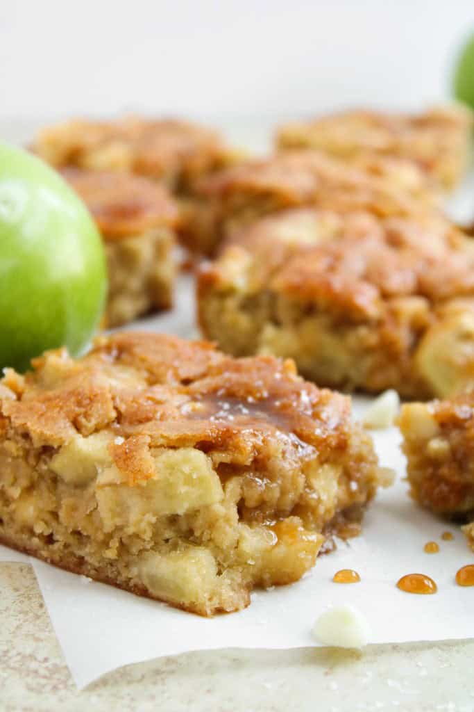 Close-up of apple blondie bars with pieces of apple visible, set on parchment paper with green apples in the background.
