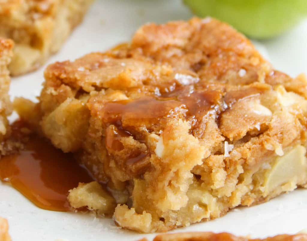 A close-up of a caramel apple blondie bar with visible apple chunks and a drizzle of caramel sauce on top.