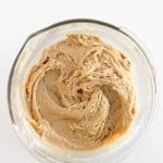 A glass mixing bowl filled with light brown cookie dough, swirled and ready for baking, sits on a white surface.