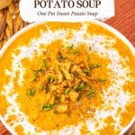 A bowl of creamy sweet potato soup topped with crispy onions and chopped chives, placed on a woven surface.