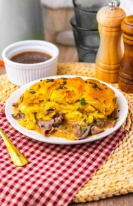 A plate of beef pot pie topped with golden crust, served with a side of brown gravy; salt and pepper shakers in the background.