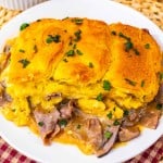 A plate with a slice of casserole topped with golden biscuit crust, containing roast beef and gravy, garnished with chopped parsley.