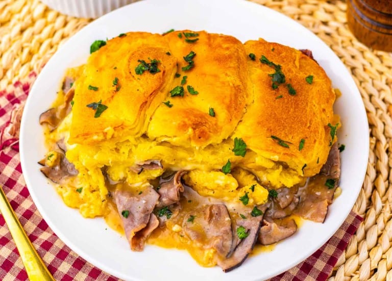 A plate with a slice of casserole topped with golden biscuit crust, containing roast beef and gravy, garnished with chopped parsley.