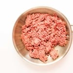 Raw ground beef&mdash;perfect for creating flavorful jalape&ntilde;o popper sliders&mdash;sits in a stainless steel frying pan on a white background.