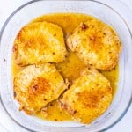 Four maple dijon pork chops sit in a glass baking dish, covered with a golden sauce.