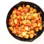 A black skillet filled with cooked diced potatoes, sliced carrots, and onions on a white background.