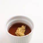 A small white ramekin containing brown liquid and a dollop of mustard on top, set against a plain white background.