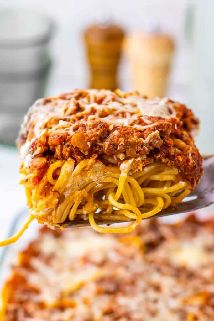 A close-up of a slice of Million Dollar Spaghetti with meat sauce and melted cheese being lifted from a casserole dish.