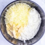 A metal bowl containing shredded cheese, grated parmesan, cottage cheese, and ricotta cheese on a white surface&mdash;perfect ingredients for making Million Dollar Spaghetti.