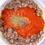 Ground beef, chopped onions, tomato sauce, and dried herbs simmer together in a white skillet on a light countertop&mdash;the perfect start for Million Dollar Spaghetti.