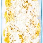 Uncooked spaghetti topped with a layer of creamy white cheese mixture in a clear rectangular glass baking dish, ready to become a classic Million Dollar Spaghetti casserole.