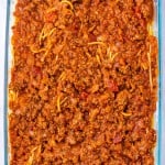 A glass baking dish filled with baked Million Dollar Spaghetti, topped with a thick layer of ground beef and rich tomato meat sauce.