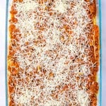 A glass baking dish filled with unbaked lasagna, reminiscent of Million Dollar Spaghetti, topped with savory meat sauce and a generous layer of shredded cheese.