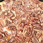 Close-up of a baked dessert topped with whole pecan halves, showing a caramelized and slightly glossy surface.