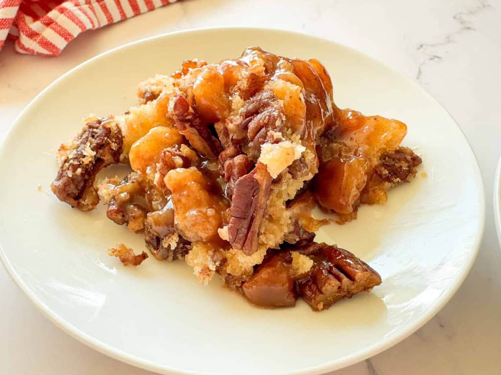 A serving of pecan cobbler with a crumbly topping and caramel sauce on a white plate.