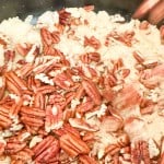 Chopped pecans being mixed into a pot of rice.