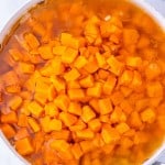 A pot filled with diced sweet potatoes boiling in water on a marble countertop.