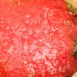 Ground meat and chopped vegetables in a pot topped with a layer of tomato sauce, being prepared for cooking.