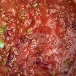 A close-up of chili with ground beef, kidney beans, tomatoes, green peppers, and onions in a pot.