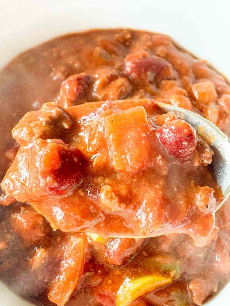 A close-up of a spoonful of chunky chili with beans, tomatoes, and ground meat in a thick red sauce.