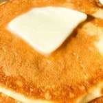 A close-up of a stack of golden buttermilk pancakes topped with a melting pat of butter.