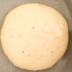 A close-up of buttermilk pancake batter cooking on a pan, showing small bubbles forming on the surface.