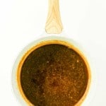 A white saucepan with a light wooden handle contains a brown liquid sauce, perfect for drizzling over Honey Glazed Ham, viewed from above on a white background.