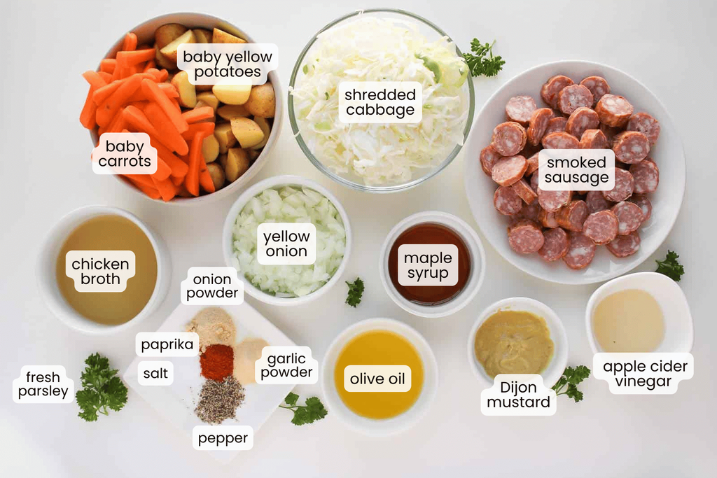 Various labeled ingredients&mdash;including chopped vegetables, smoked sausage, spices, broth, olive oil, mustard, and vinegar&mdash;are arranged in bowls and plates on a white surface.