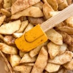 Sliced apples coated with cinnamon and sugar are mixed with a yellow spatula, just like preparing a classic old fashioned apple pie.
