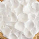 A close-up, top-down view of a pie topped with a thick, peaked layer of white meringue in a glass dish.