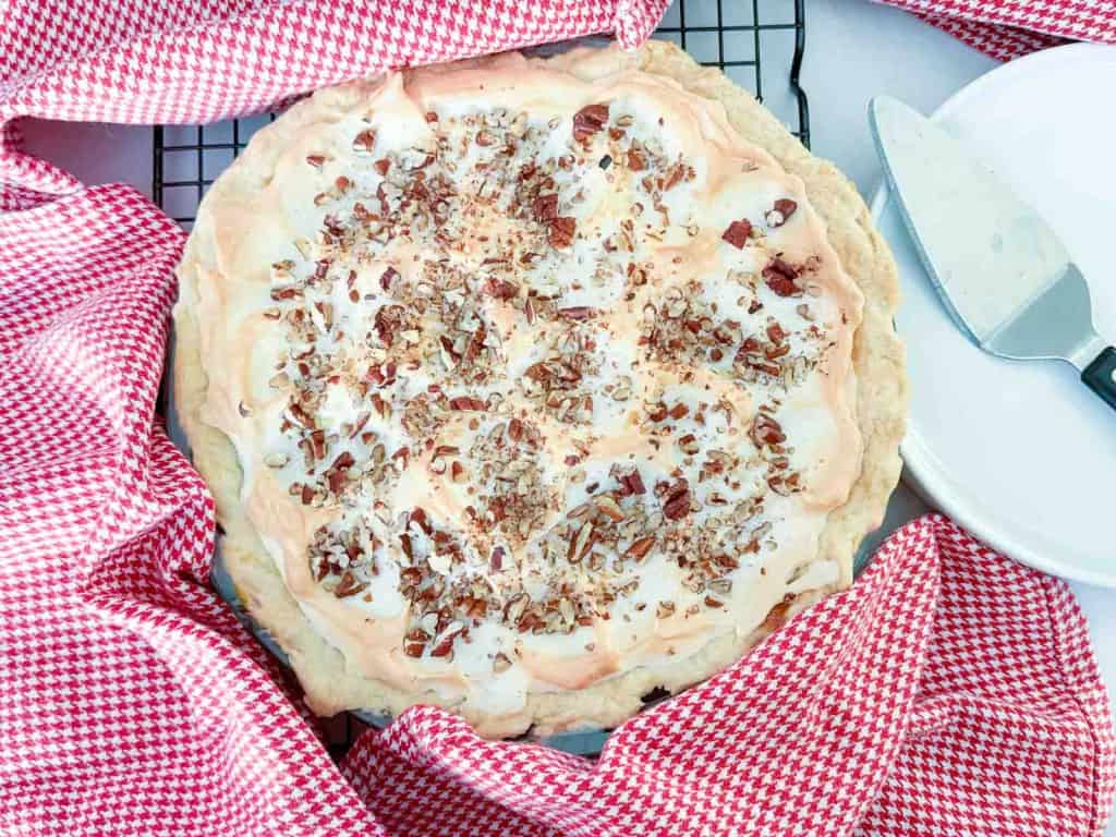 A meringue-topped pie sprinkled with chopped nuts, sitting on a wire rack next to a pie server.