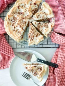 A pecan-topped meringue pie on a cooling rack, with one slice served on a plate next to a pie server and a fork.