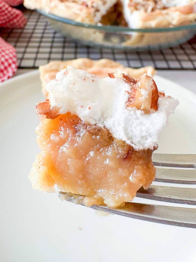 A fork holding a bite of pie topped with meringue and pecans, with the whole pie in the background.