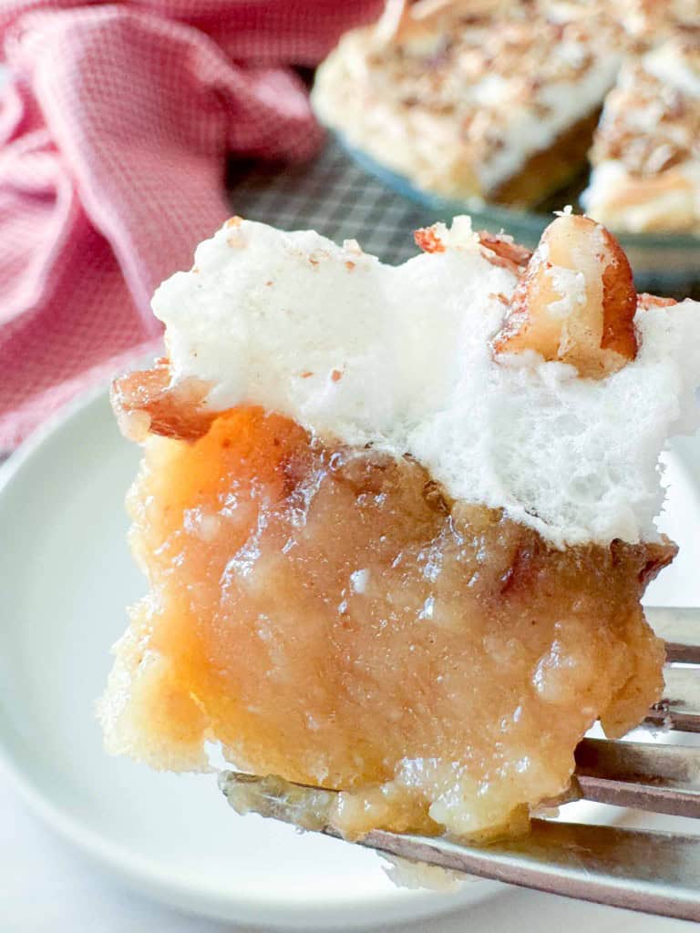 A bite of apple crisp topped with meringue and a pecan on a fork.