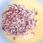Chopped pecans in a pool of beaten eggs inside a mixing bowl.