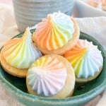 Four small, round shortbread cookies topped with swirls of rainbow-colored icing in a green ceramic bowl.