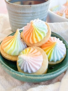 Four small, round shortbread cookies topped with swirls of rainbow-colored icing in a green ceramic bowl.