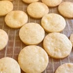 A baking sheet lined with parchment paper covered in round, golden-brown shortbread Iced Gems.