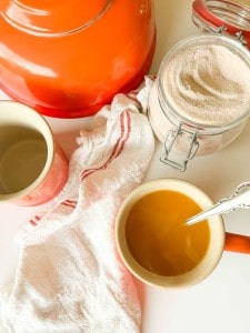 An orange kettle, two mugs, a jar of sugar, and a tea towel on a white surface.