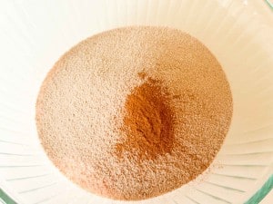 A glass bowl containing a mound of light brown flour with a small pile of cinnamon in the center.