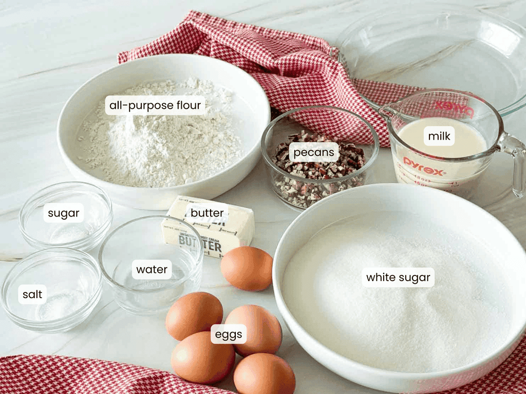 Ingredients for a 1914 pie arranged on a counter, including all-purpose flour, pecans, milk, butter, sugar, water, salt, white sugar, and eggs.
