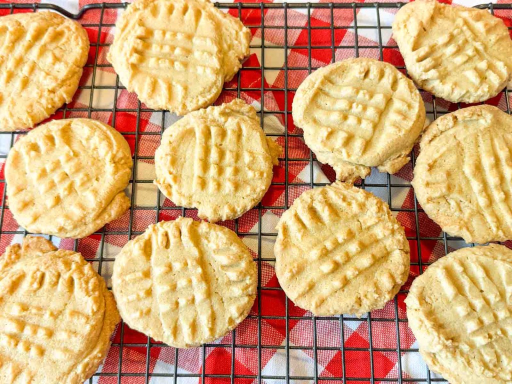 Peanut butter cookies with a crisscross fork pattern on a wire cooling rack over a red and white checkered cloth.