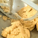 A metal stand mixer paddle mixing cookie dough in a metal bowl.