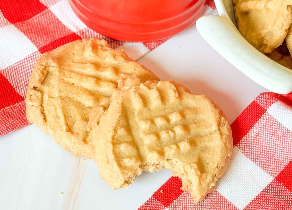 Two peanut butter cookies with crisscross patterns on a red and white checkered napkin.