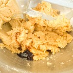 Cookie dough being mixed in a metal bowl with a drop of dark extract.